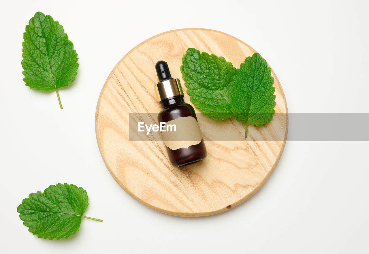 Brown glass bottle with a pipette for cosmetics and green mint leaves on a white background, top v