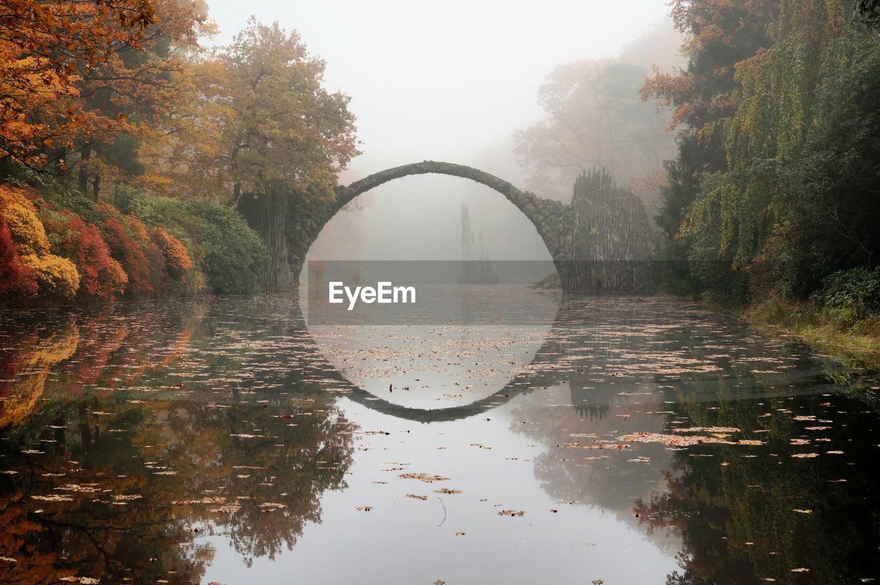 Rakotz bridge over calm lake against sky at park during autumn