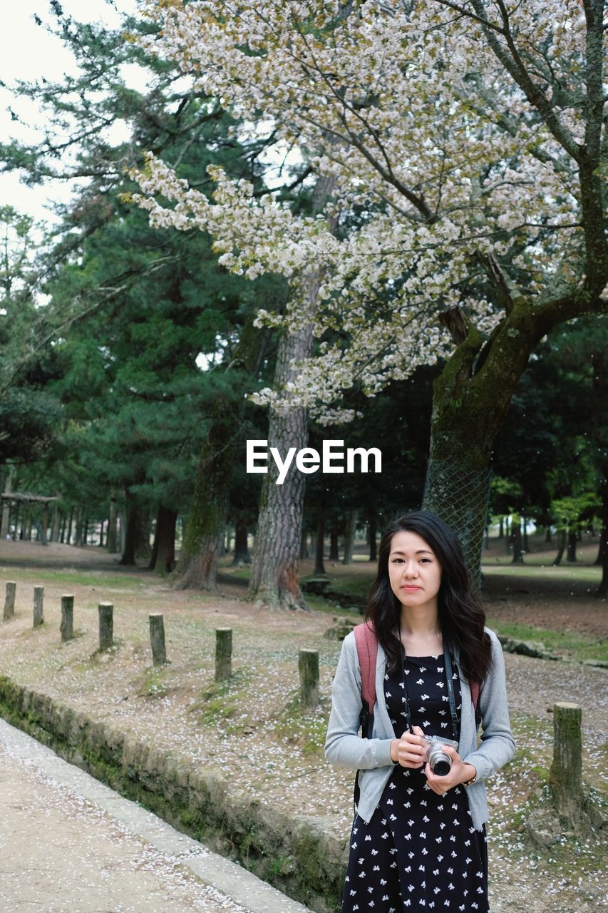 Portrait of young woman standing by tree against plants