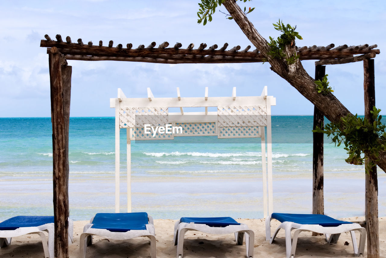 Wooden white gazebo by the beach with long chairs under it