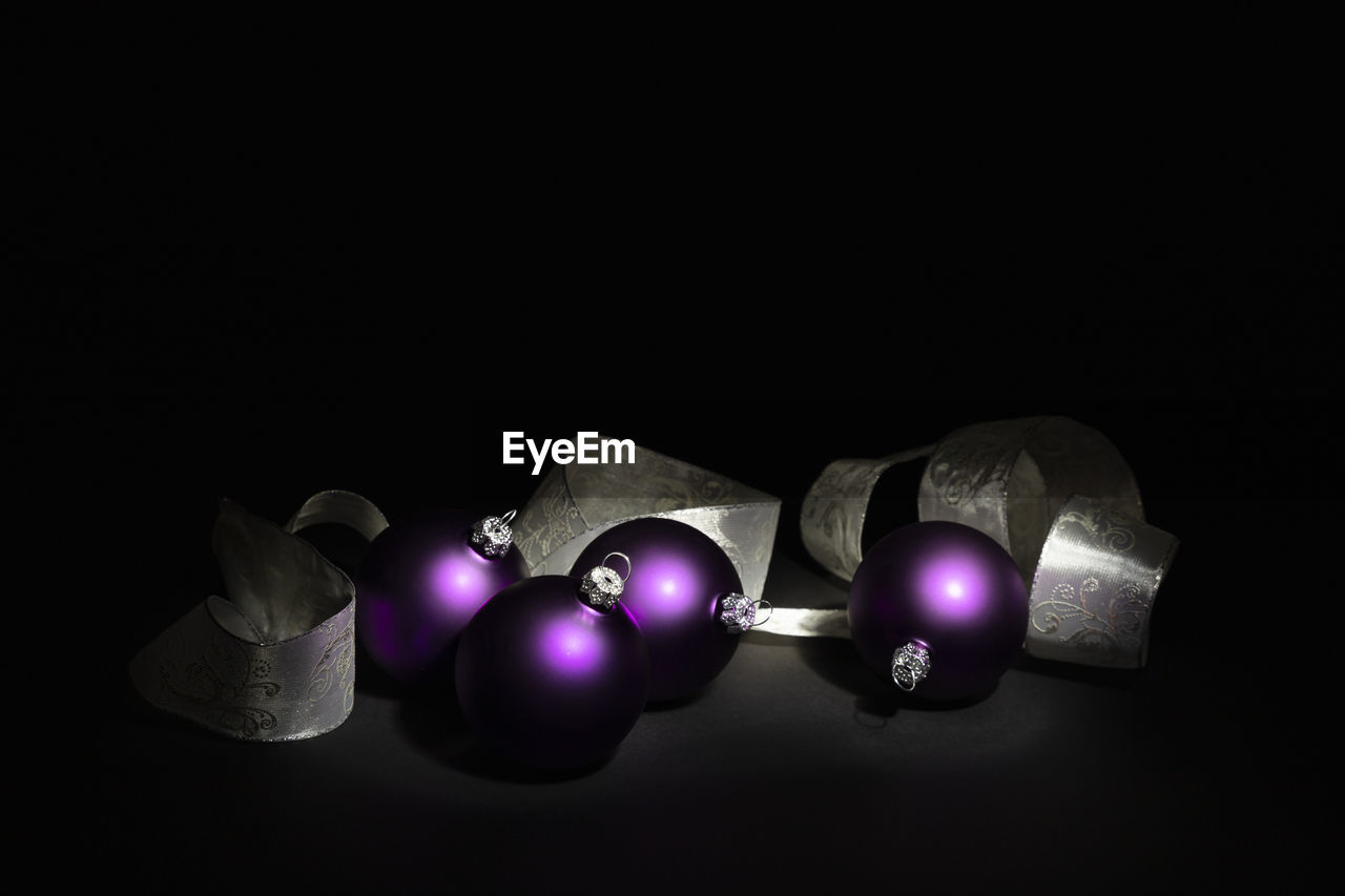 Arrangement of illuminated purple christmas balls with a silver ornate ribbon on black background