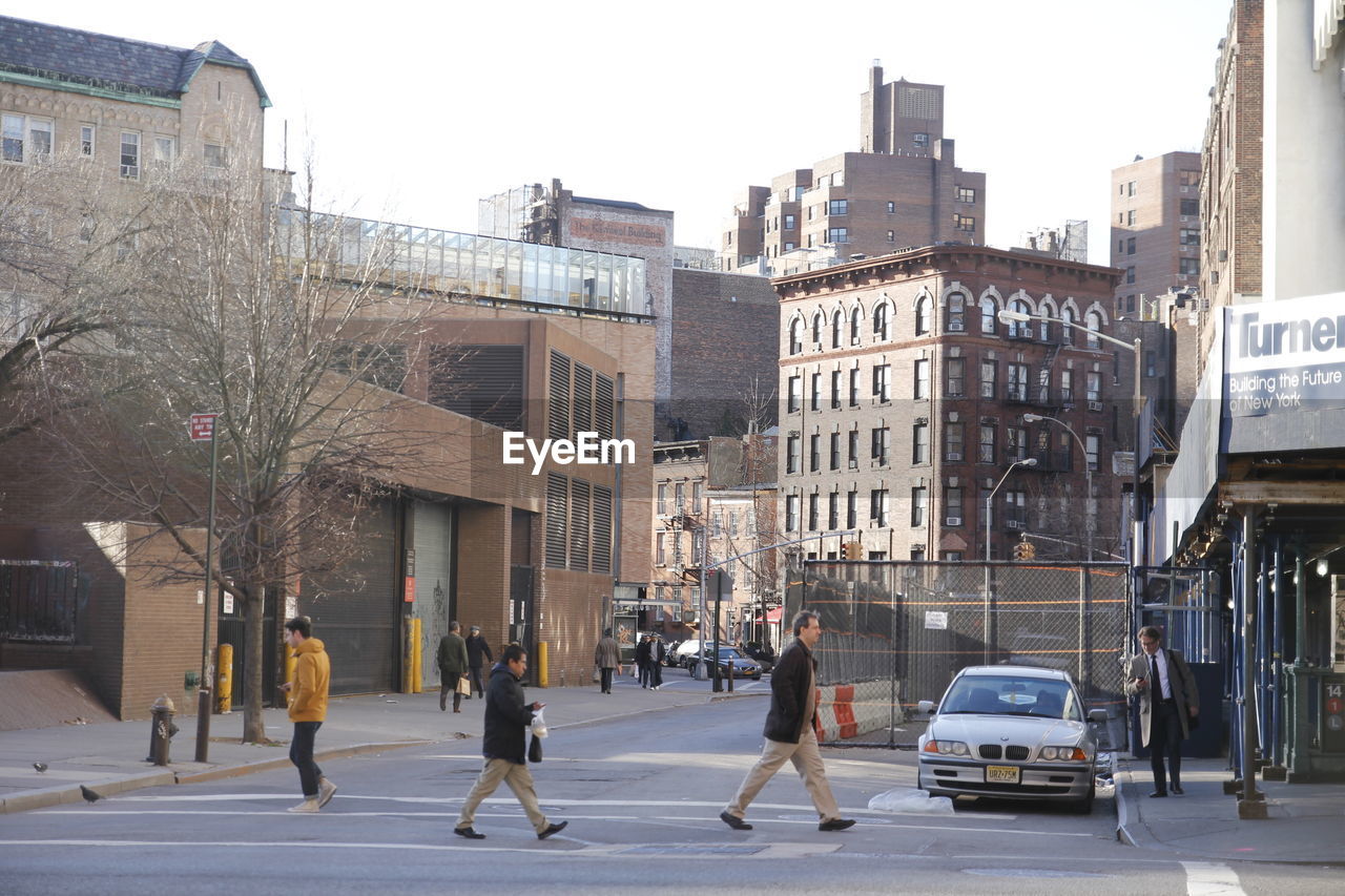 GROUP OF PEOPLE WALKING ON ROAD AMIDST BUILDINGS IN CITY