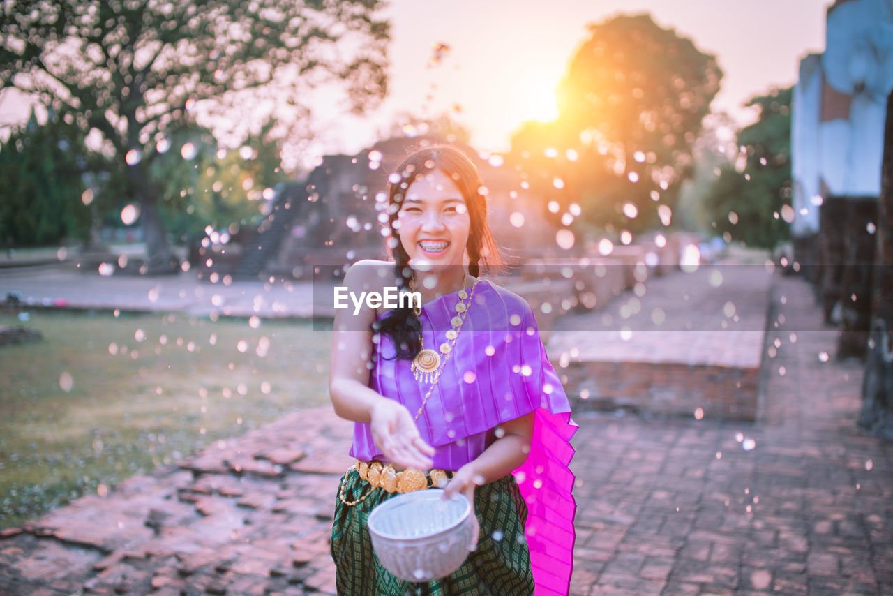 Cheerful woman in traditional clothing splashing water while standing outdoors