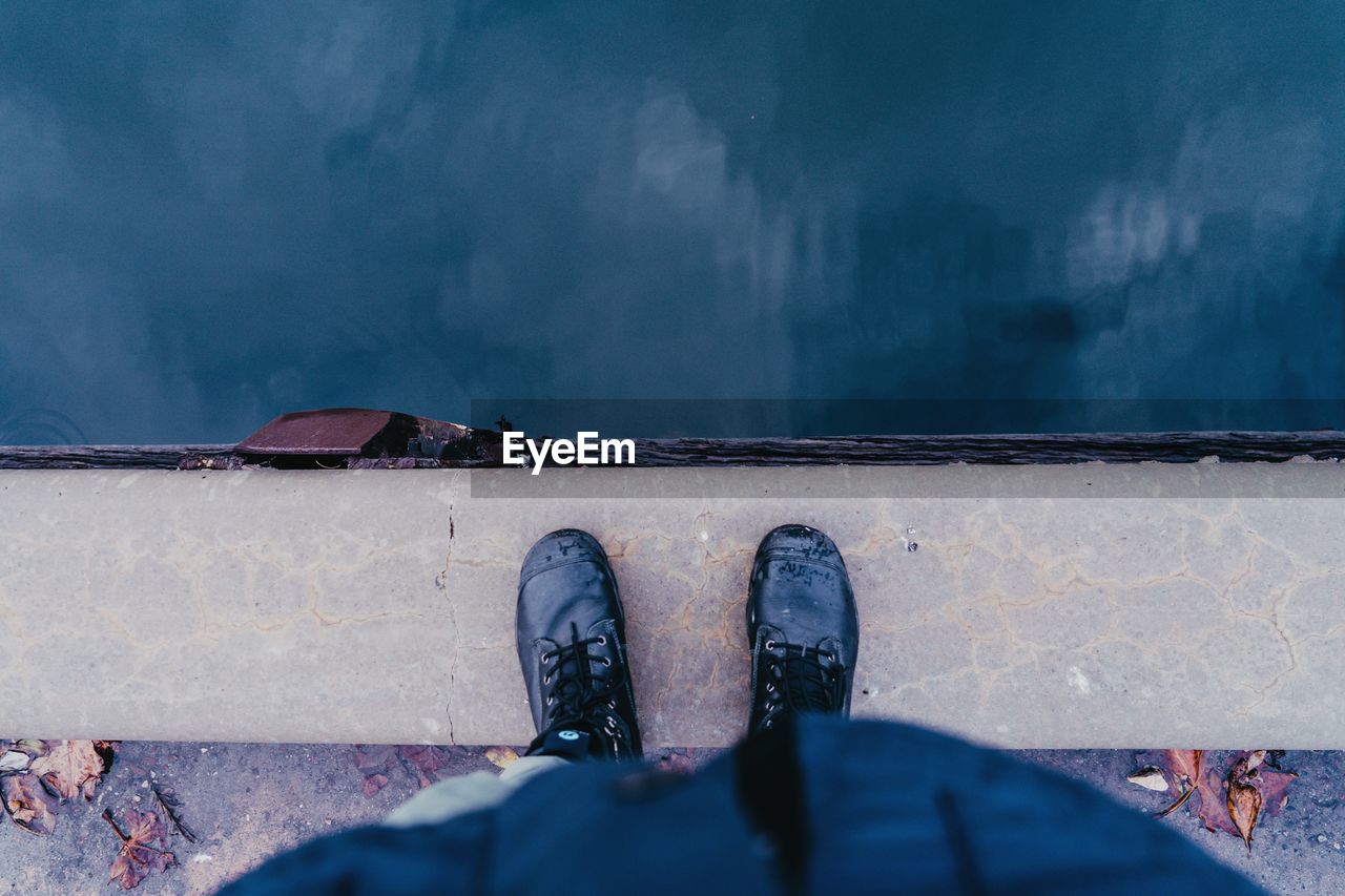 Low section of person wearing boots standing by water 