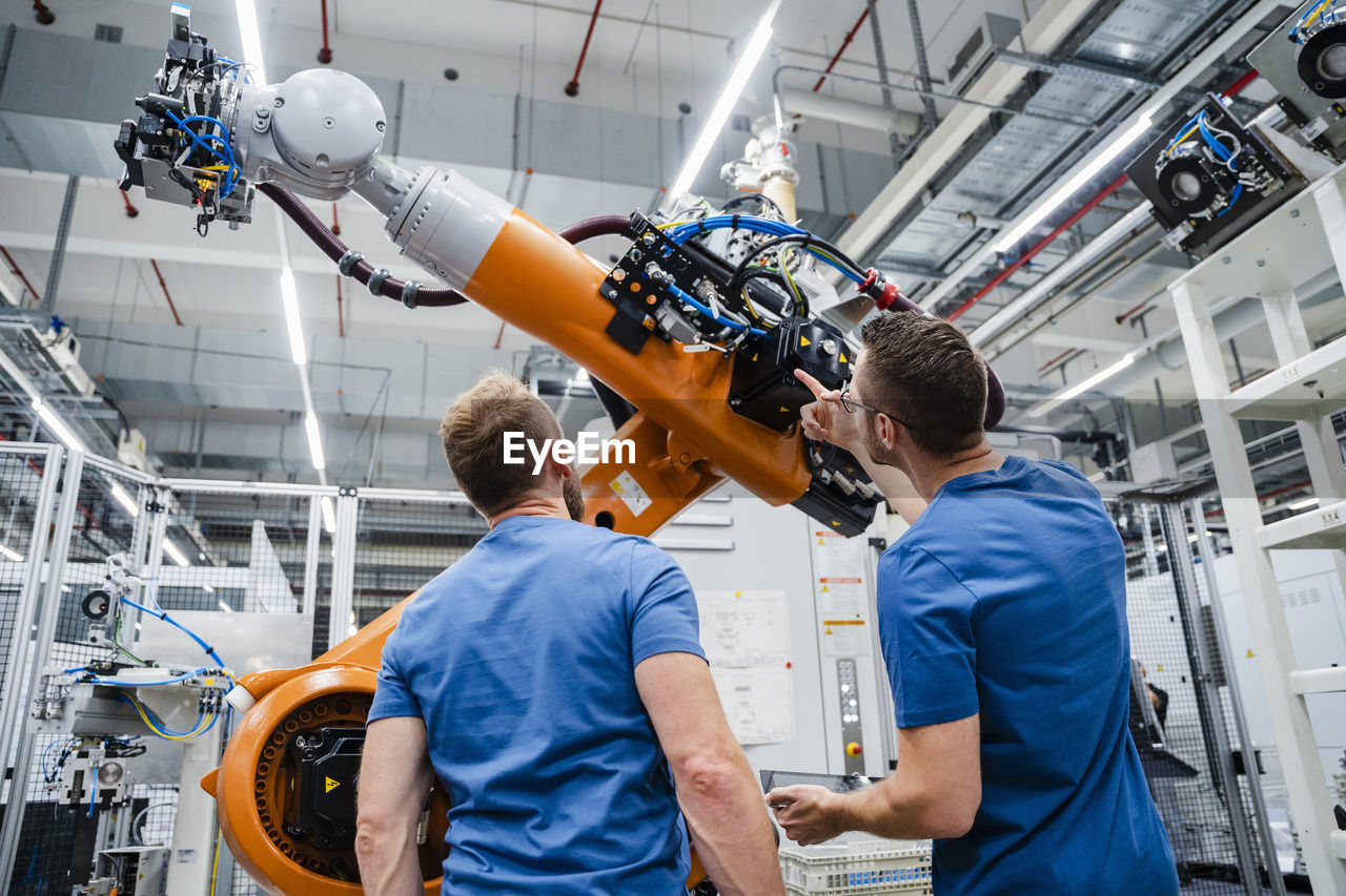 Two technicians examining industrial robot in a factory