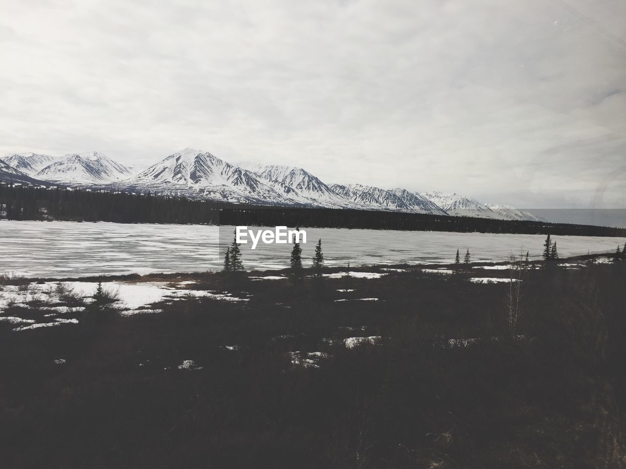 Scenic view of river by snow covered mountains against cloudy sky