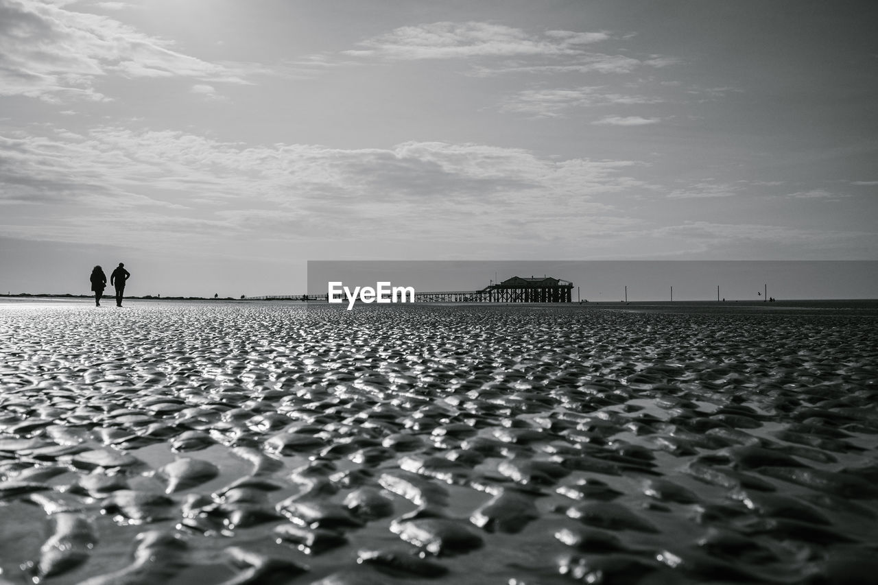 People standing on pebbles on field against sky