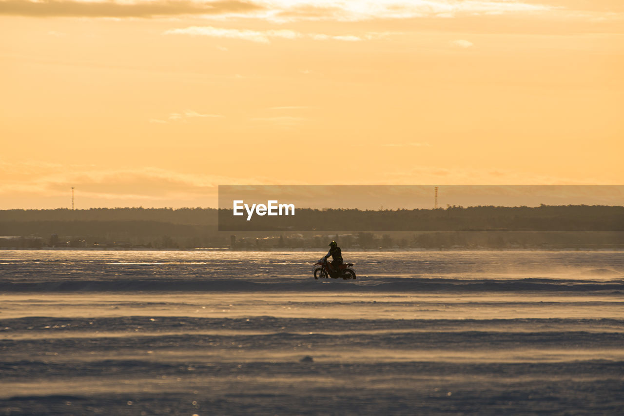 Silhouette person riding on frozen lake against sky during sunset