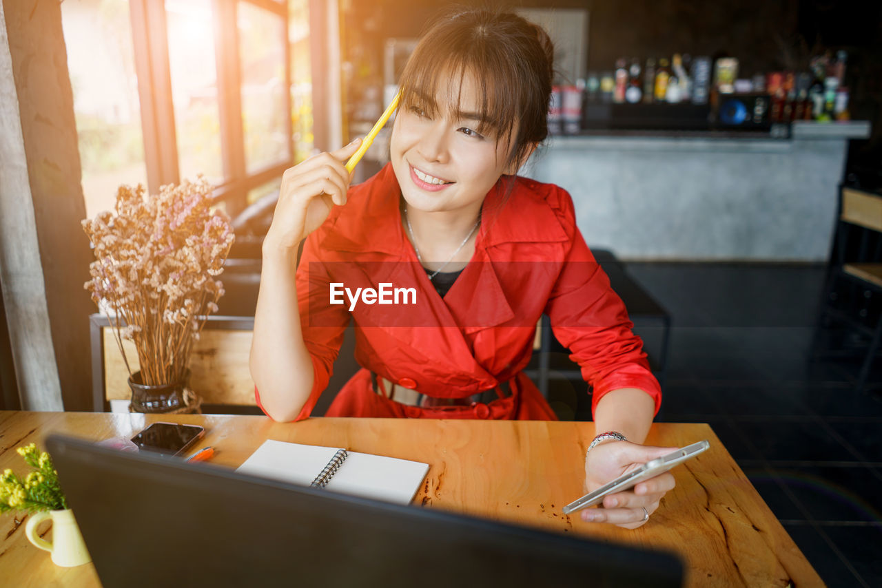 Woman looking away while holding mobile phone on table