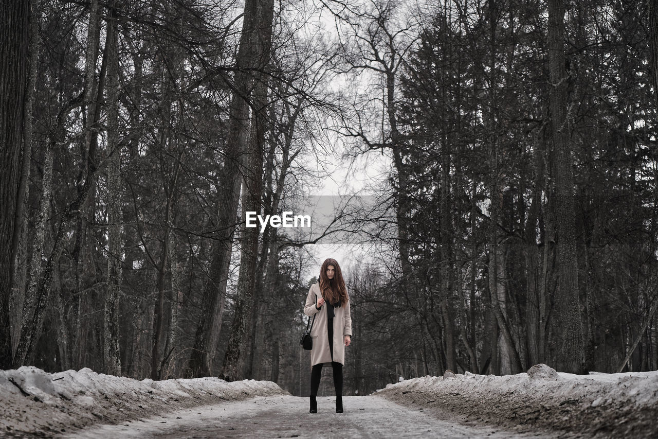 Full length of woman standing on road at forest during winter