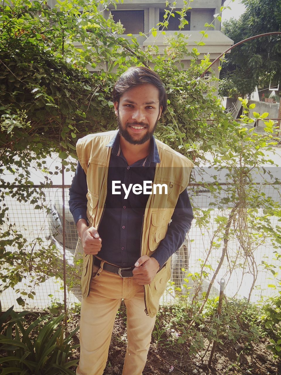 PORTRAIT OF SMILING YOUNG MAN STANDING AGAINST TREES