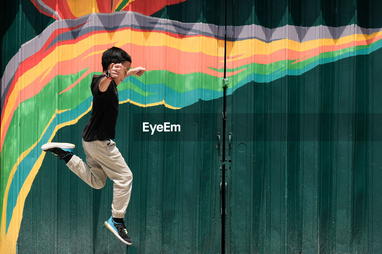 Side view of boy jumping by metallic gate