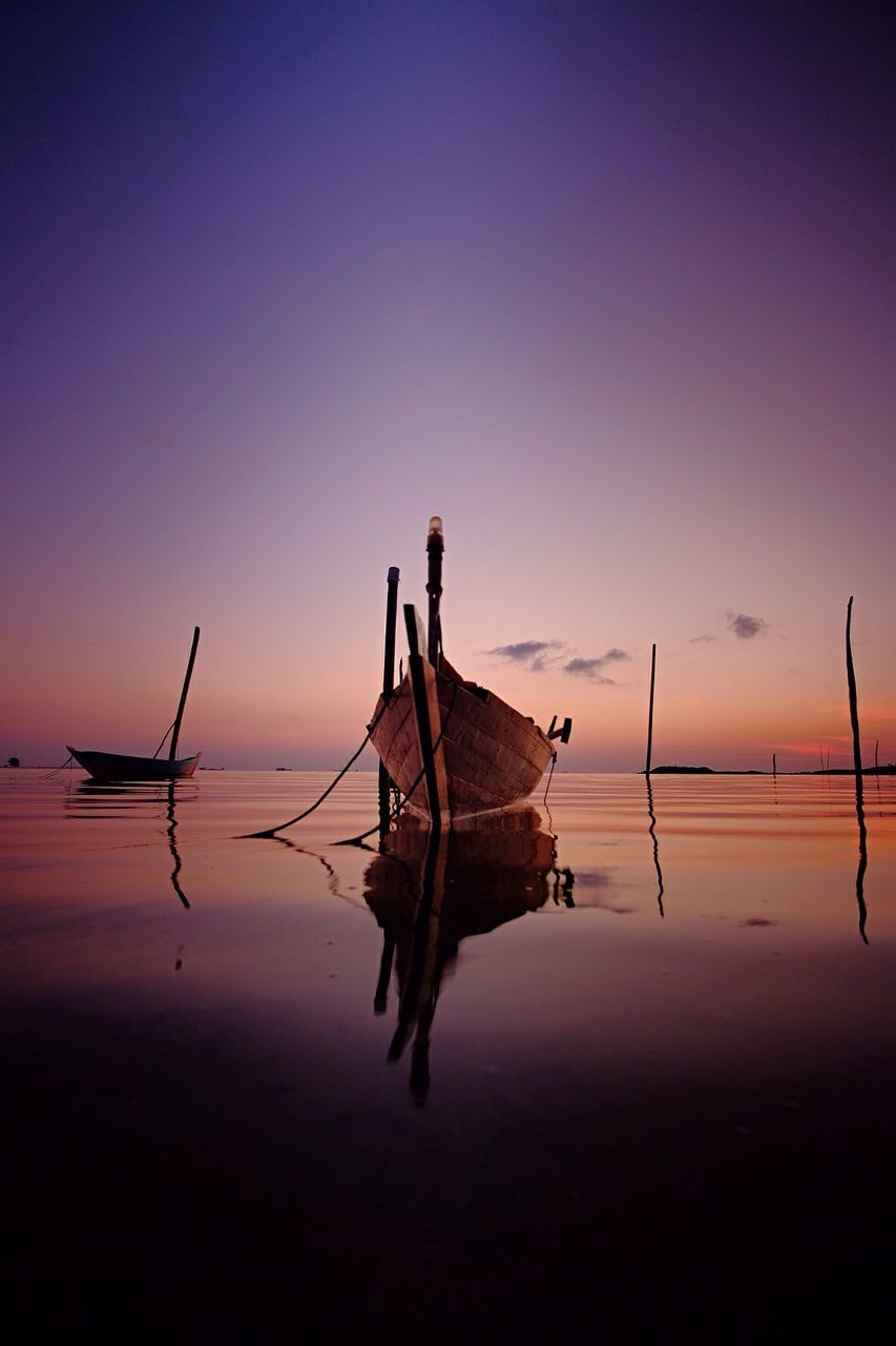 Boats moored on river against sky at sunset