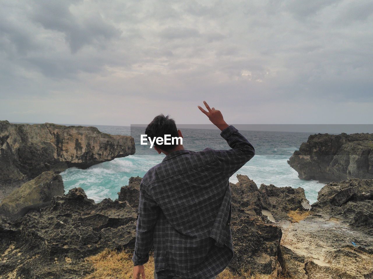 Rear view of man standing on rock by sea against sky