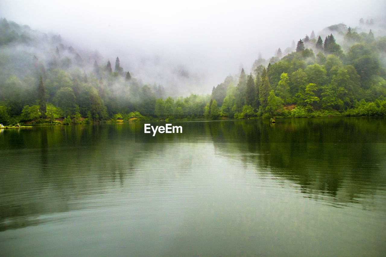 Scenic view of lake by mountains in foggy weather