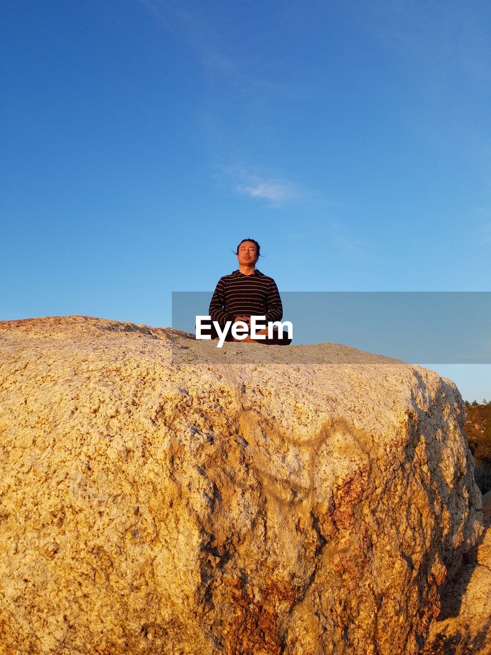 Low angle view of man meditating on rock against clear sky