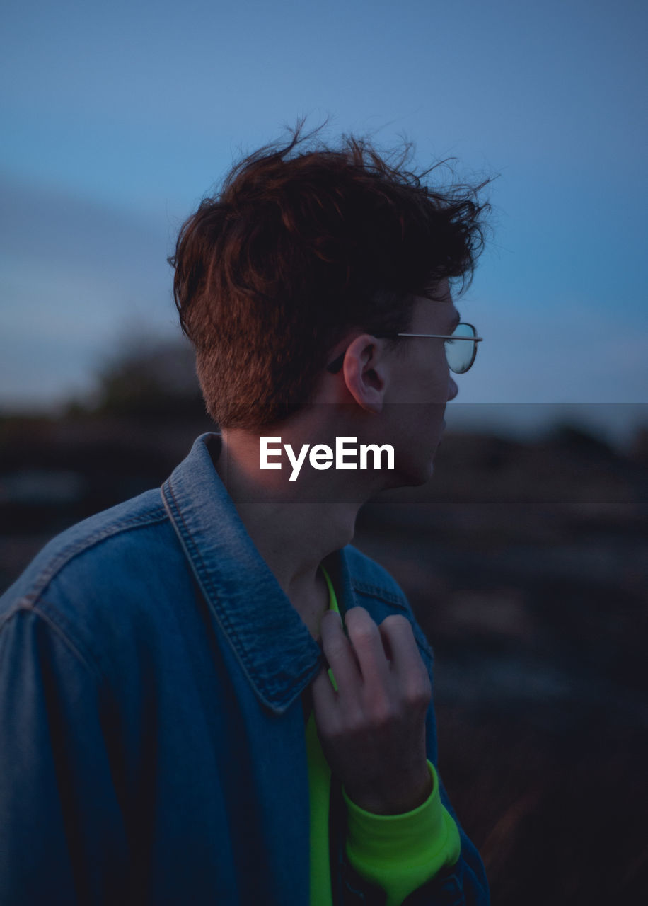 Close-up of young man looking away against sky during sunset