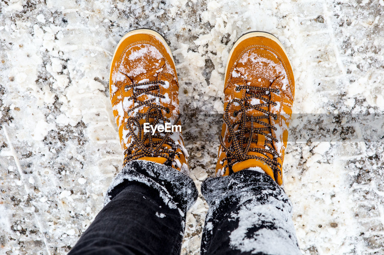 LOW SECTION OF PERSON STANDING ON SNOW COVERED