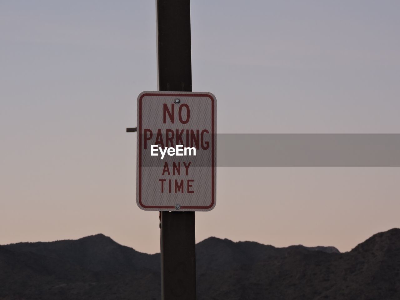 No parking sign on pole against clear sky during sunset