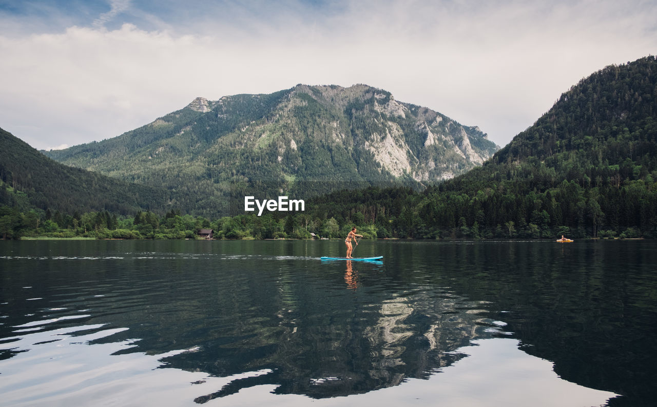 Woman paddleboarding in lake by mountains against sky