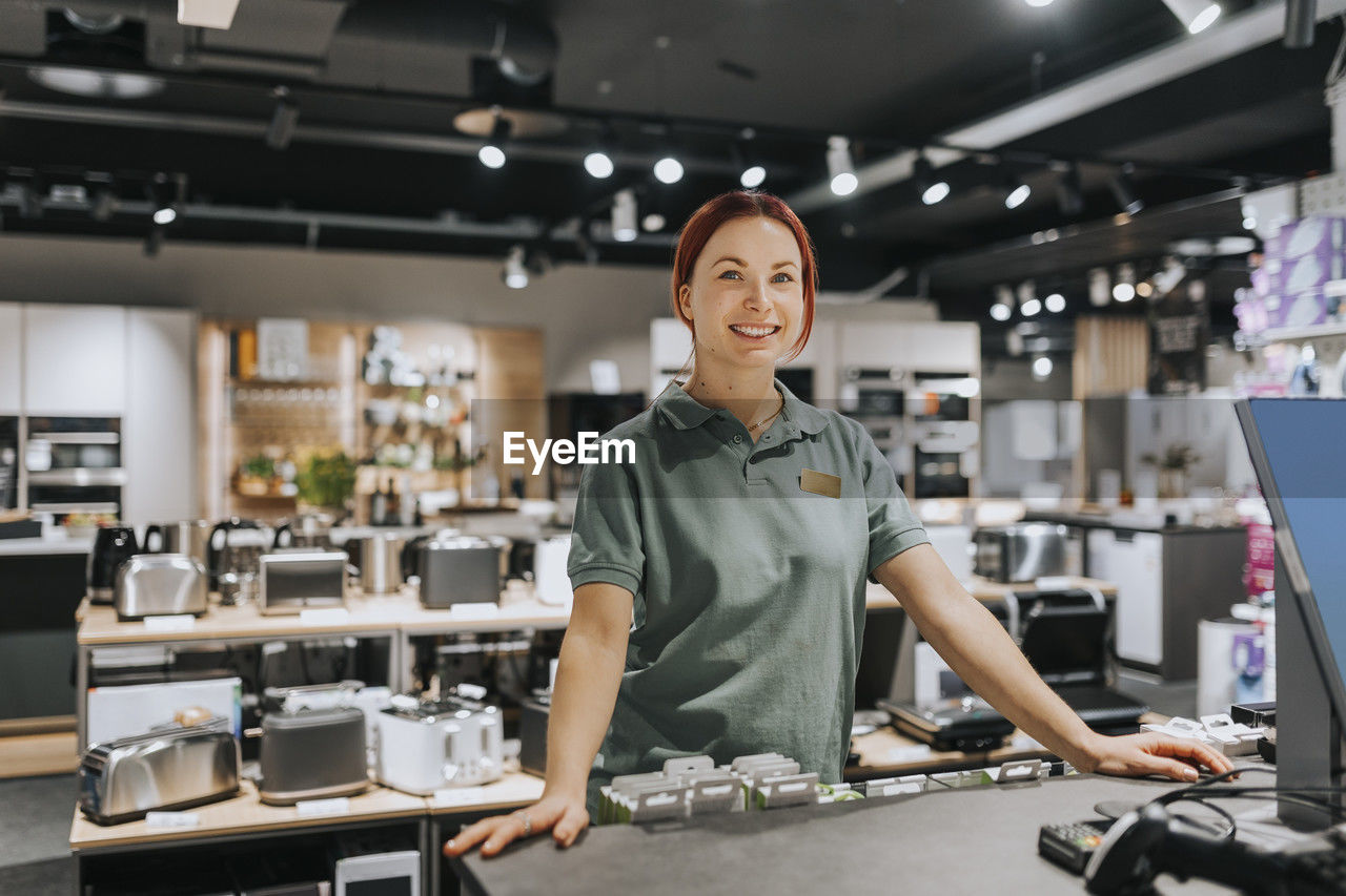 Portrait of smiling female sales clerk standing at counter in electronics store