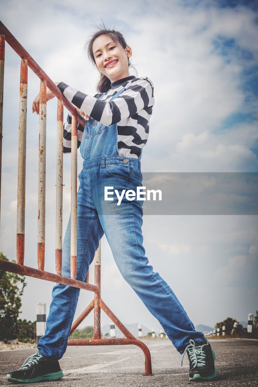  portrait of smiling young woman standing against sky and caught a fence