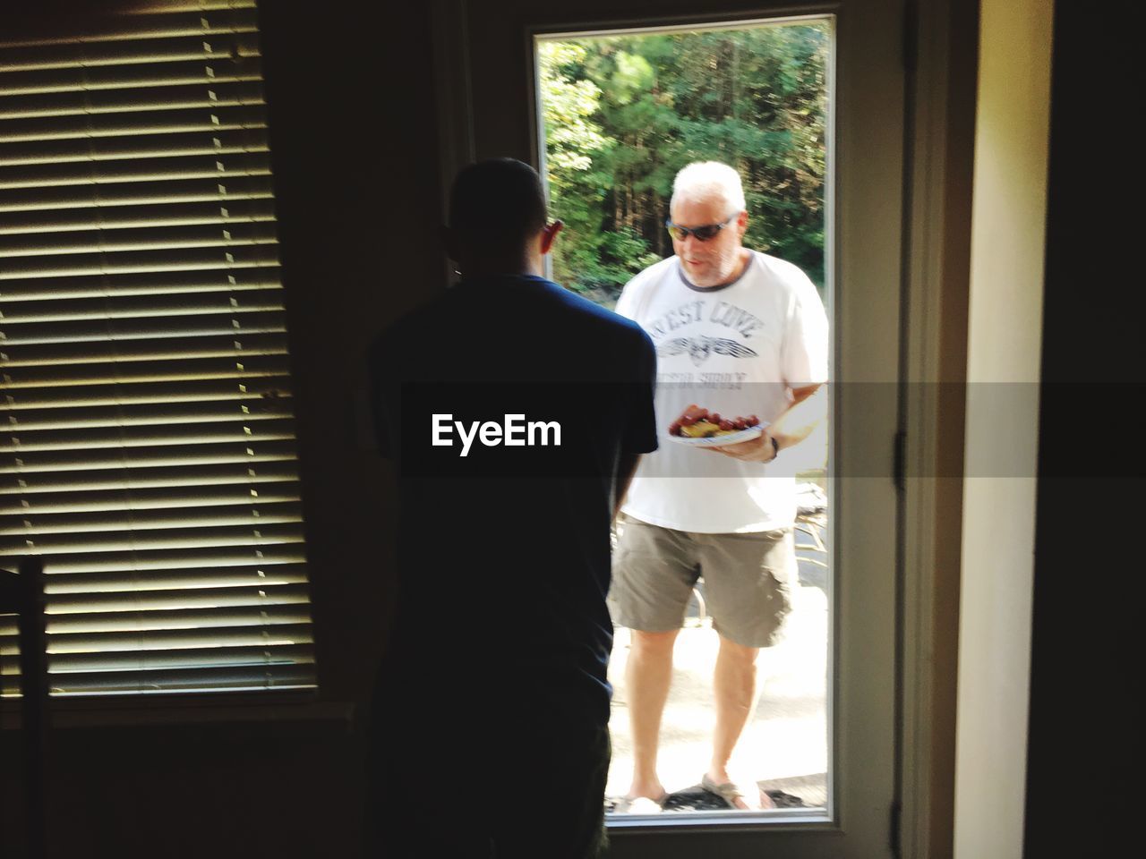 REAR VIEW OF MAN STANDING BY WINDOW