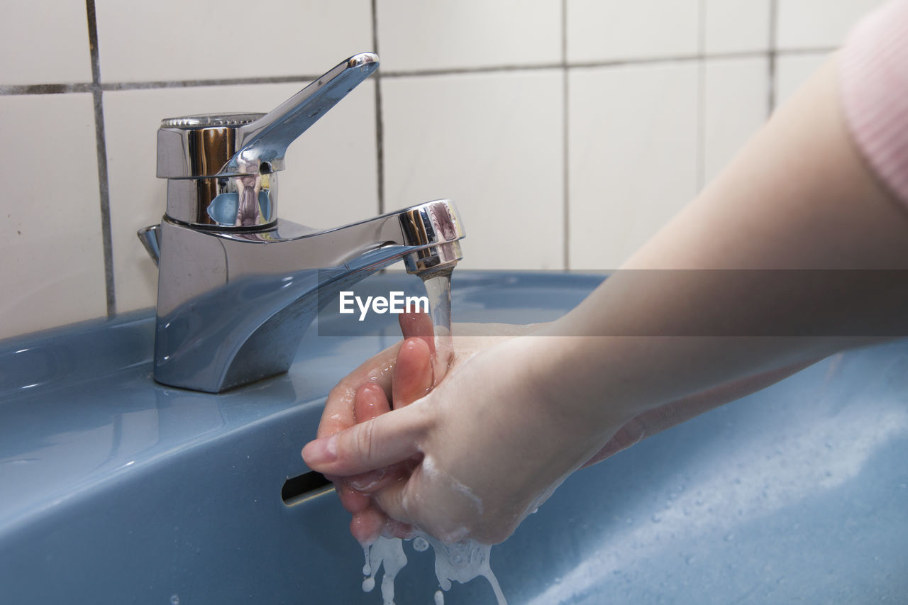 Cropped hands of woman washing hands at sink