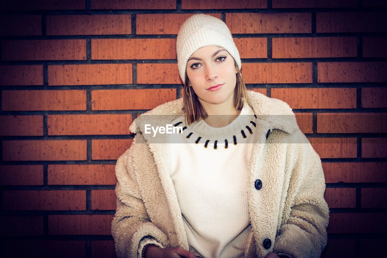 Portrait of woman standing against brick wall