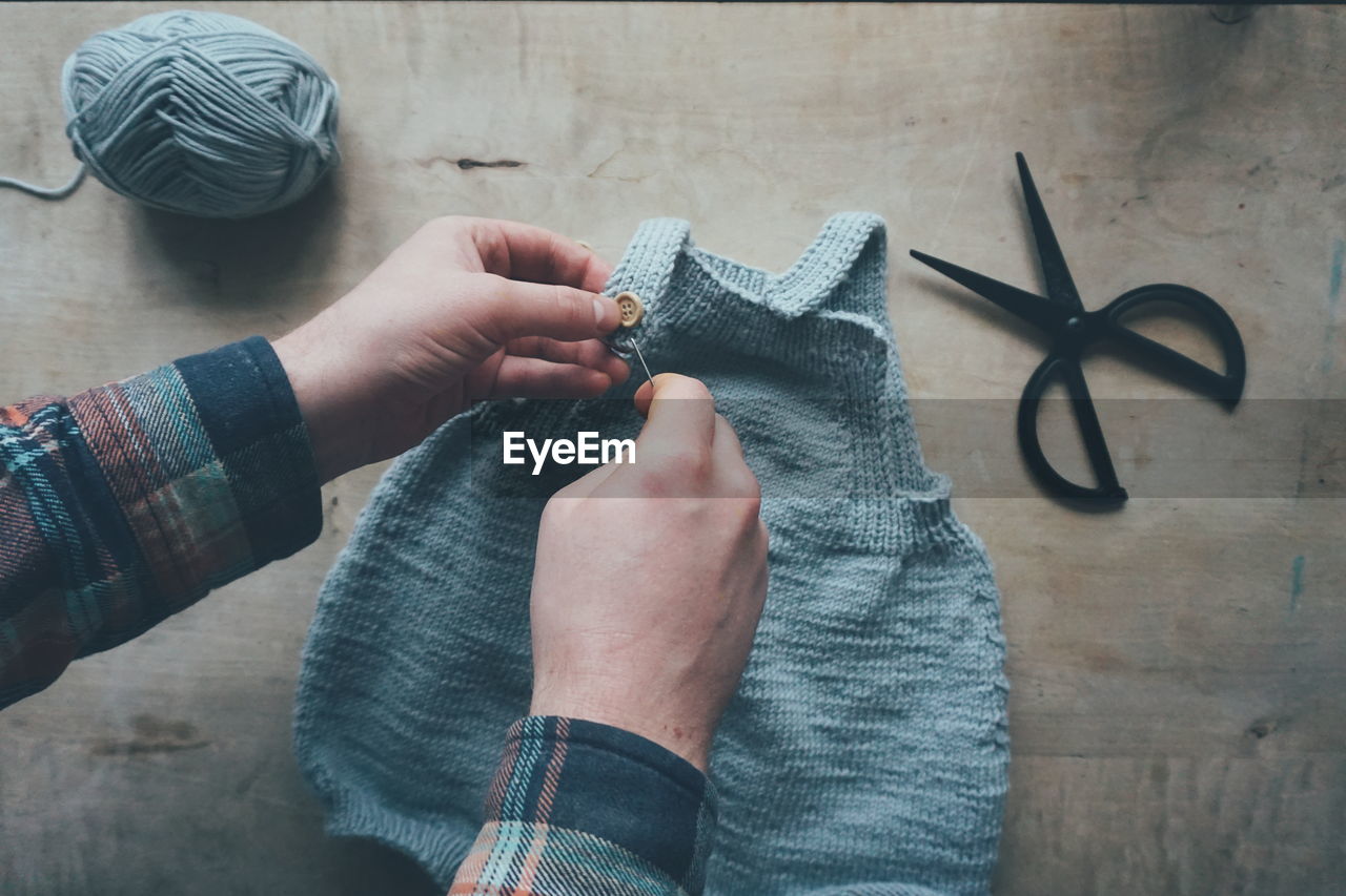 High angle view of hand sewing buttons on knitted baby cloth