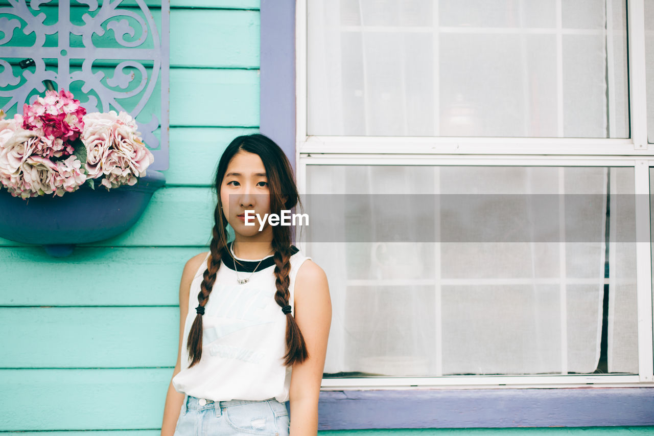 Portrait of beautiful young woman standing against house