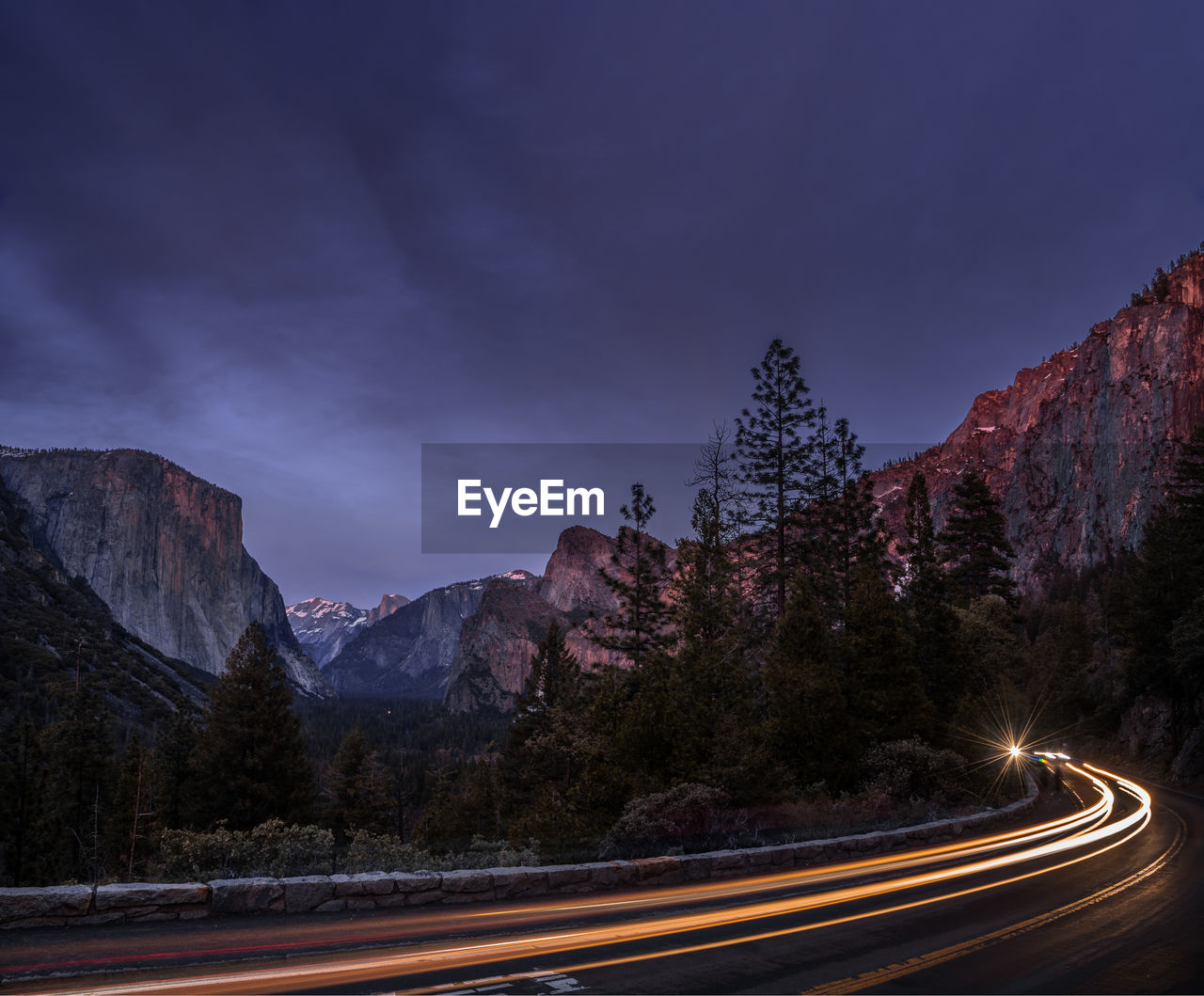 Light trails on road by mountains against sky at night