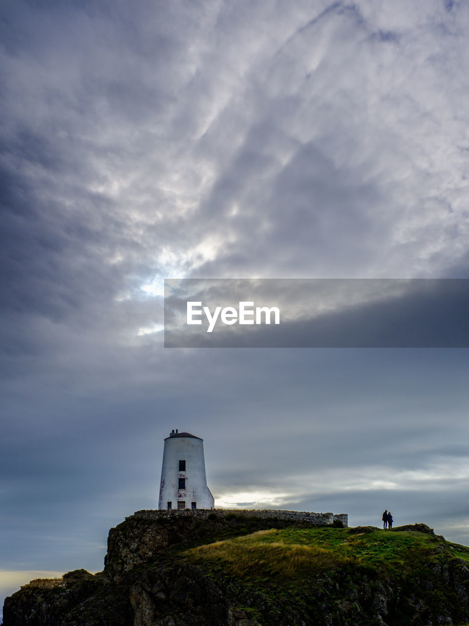 lighthouse by sea against cloudy sky