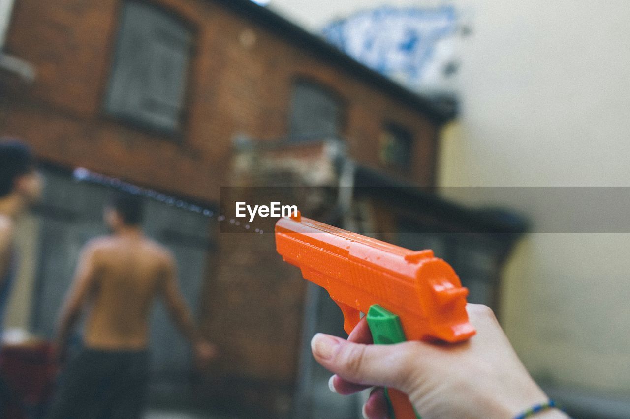 Cropped hand holding orange water gun by building