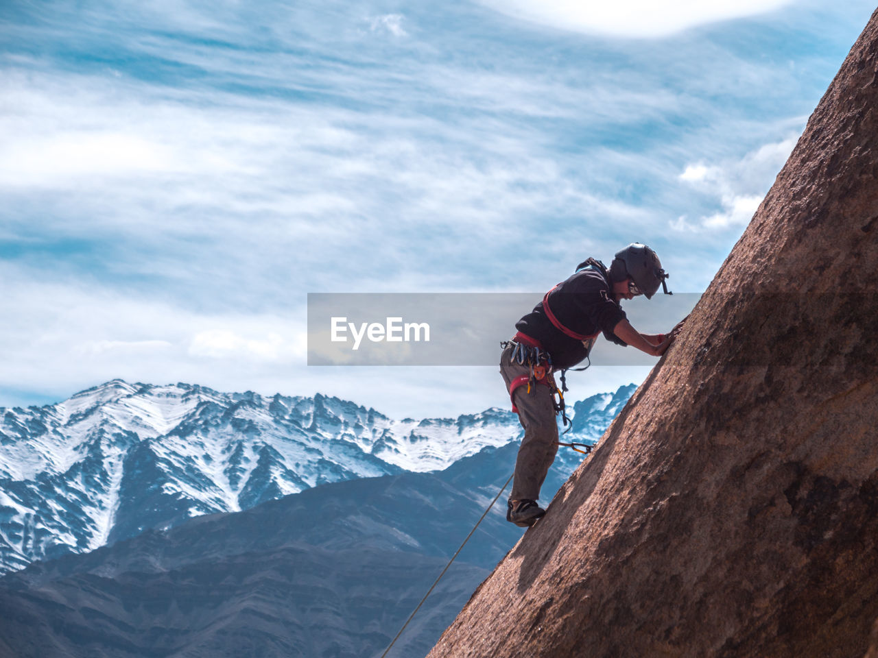 Man climbing on rock formation against snowcapped mountains