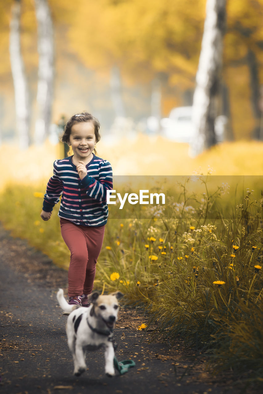 Smiling girl with dog running on road