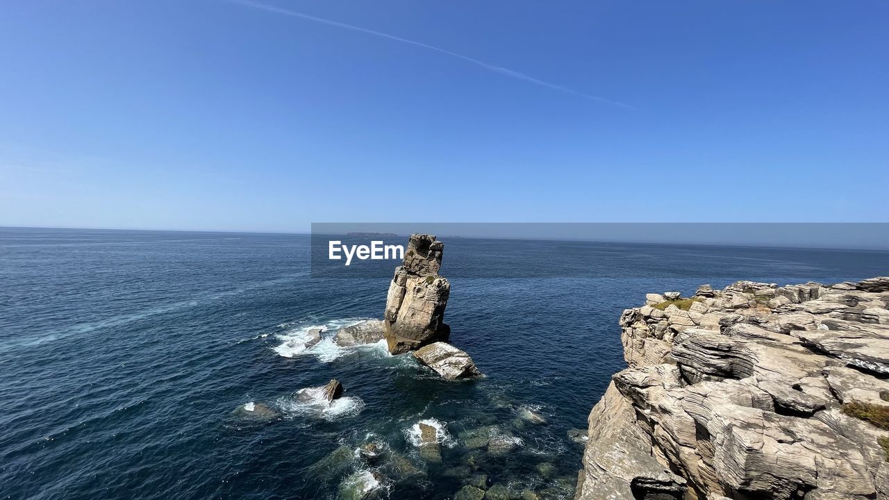 Rocks in sea against clear blue sky