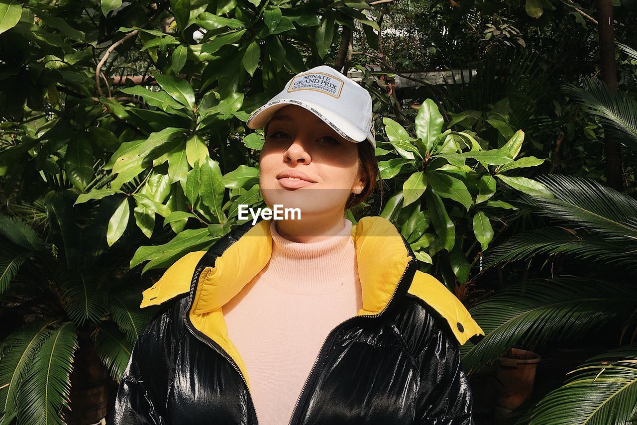 Portrait of young woman standing against plants