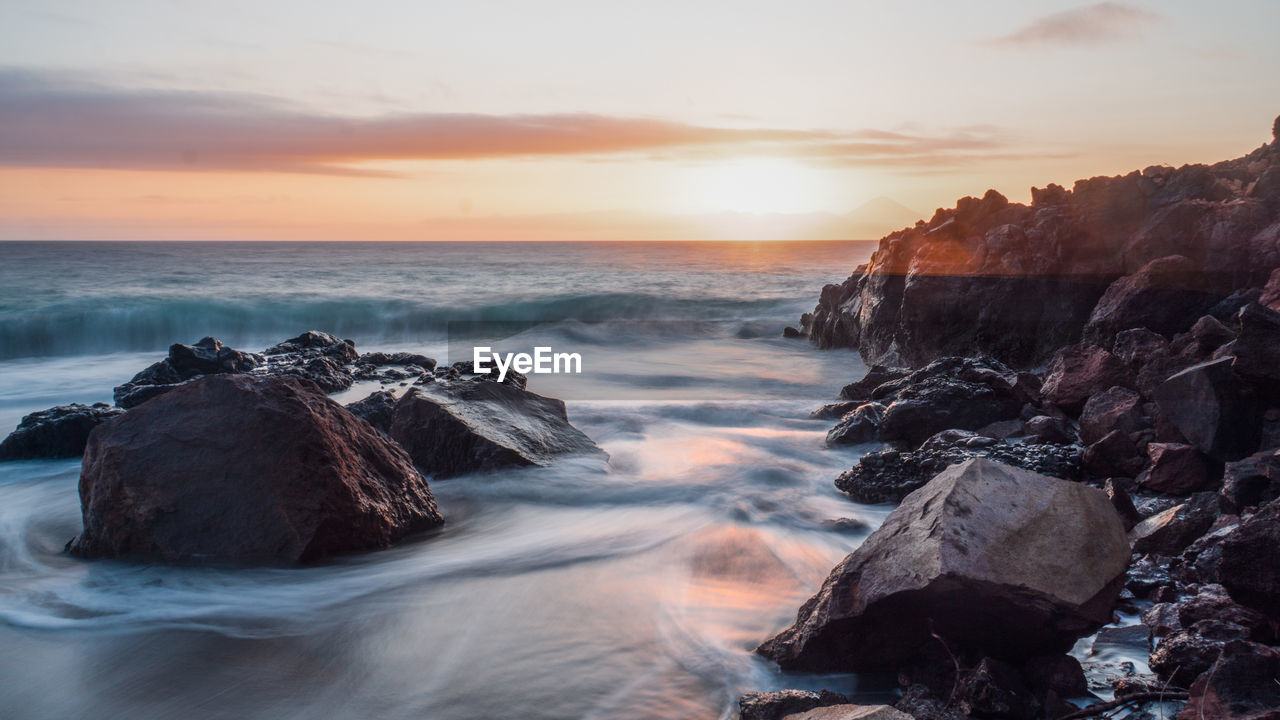 Scenic view of rocks in sea against sky during sunset