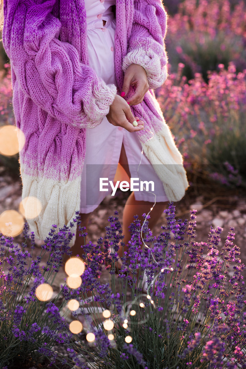 Woman wearing stylish knitted cardigan posing in lavender field picking flowers outdoors. 