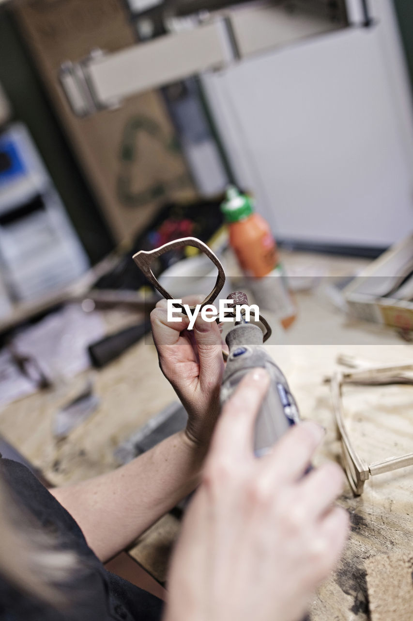 Cropped image of female owner making eyeglasses with work tool at workshop