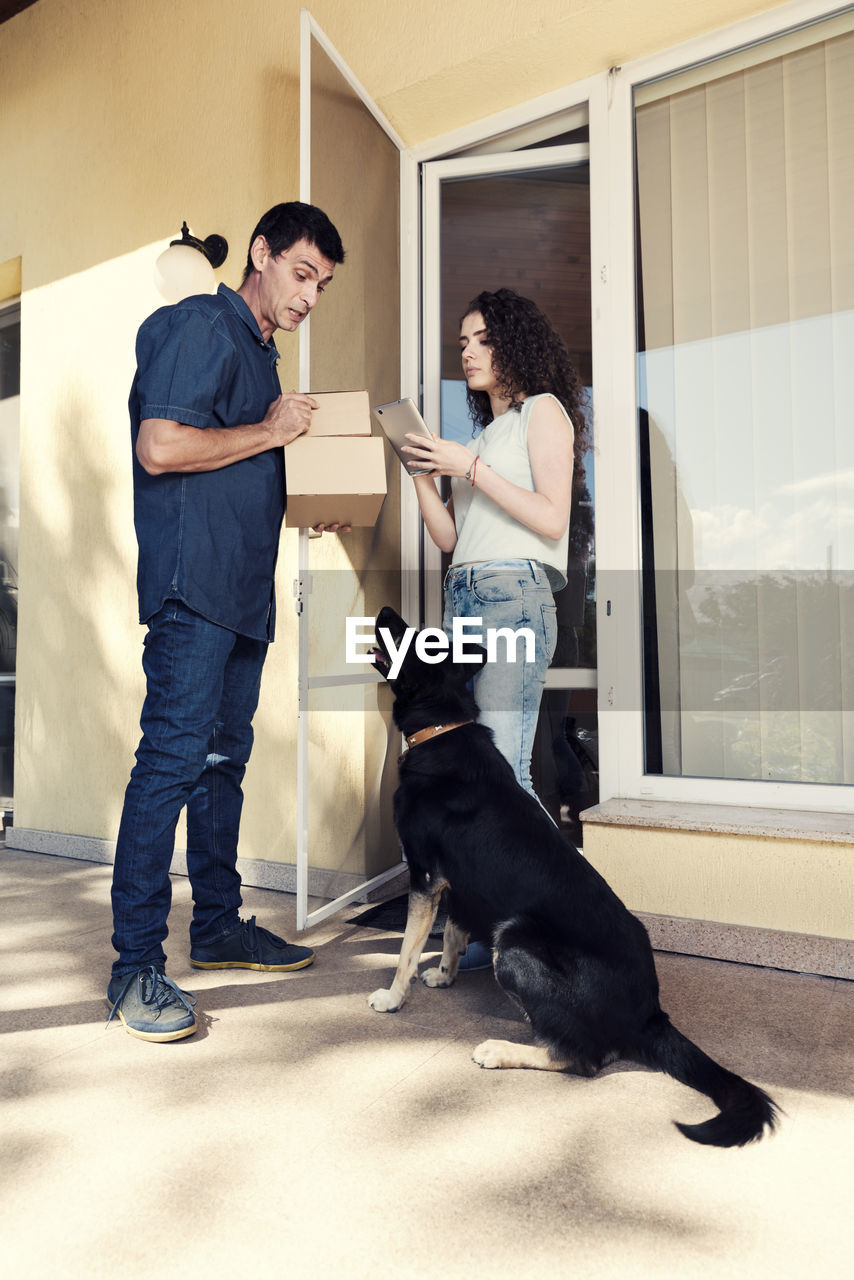 Woman signing on digital tablet while delivery man looking at dog against house