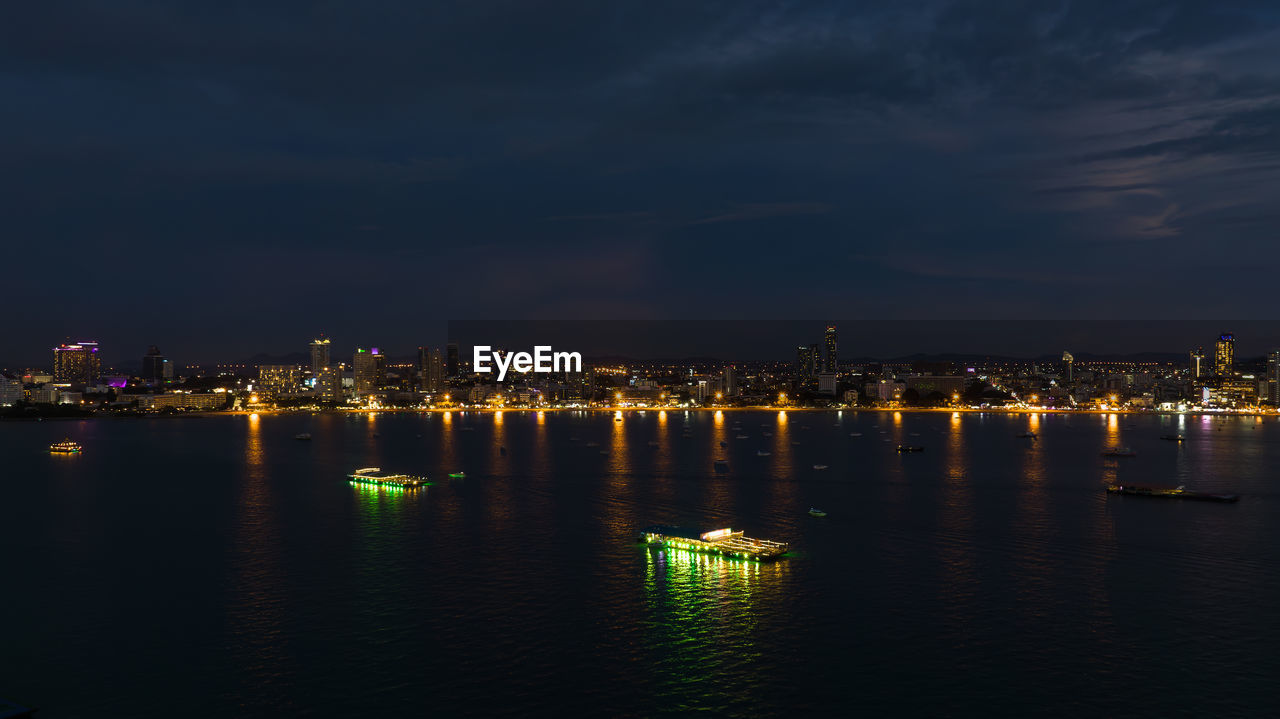 illuminated city at waterfront against sky at night