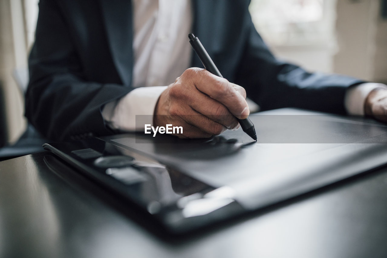 Close-up of businessman using graphics tablet at desk in office