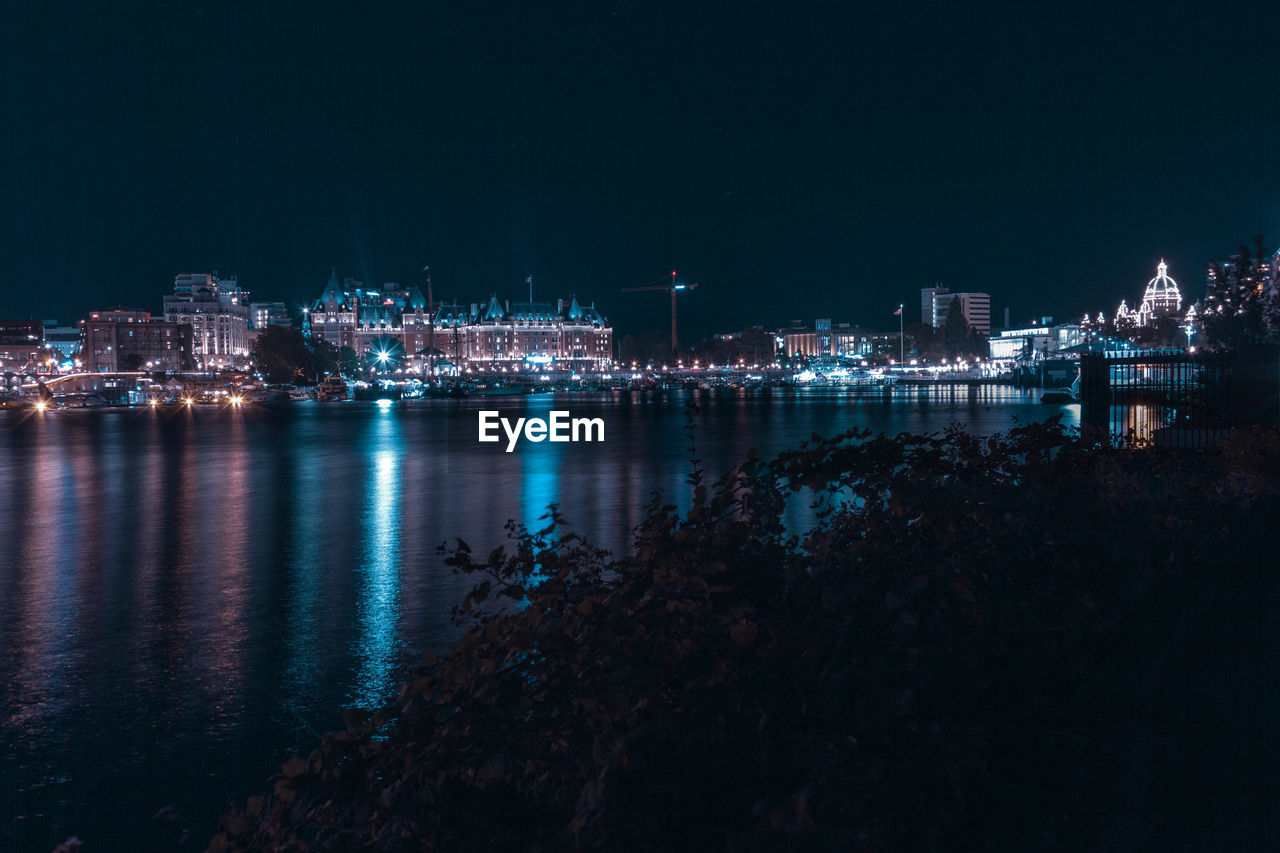 ILLUMINATED CITY BY SEA AGAINST SKY AT NIGHT