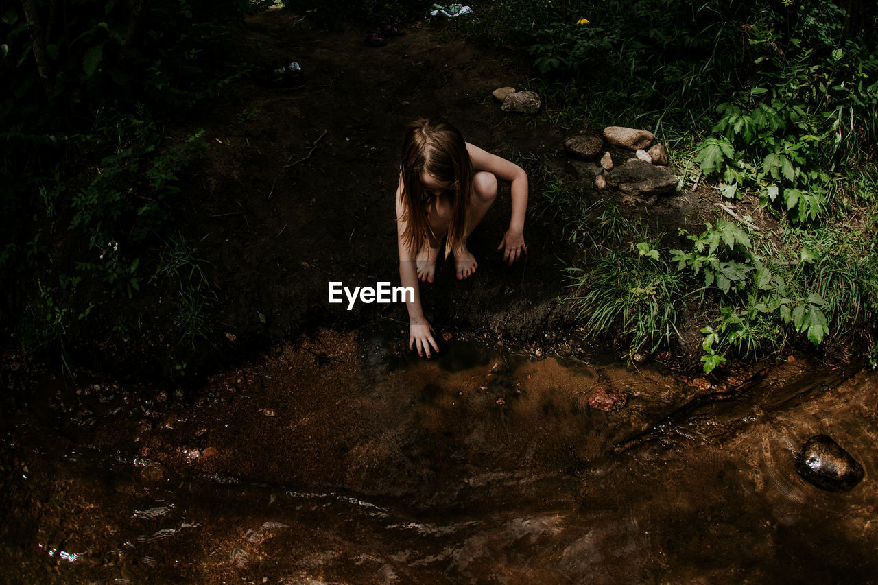 Overhead of young girl playing in the mud on the bank of a river