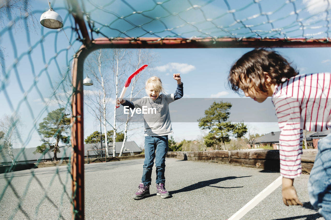 Excited girl gesturing while playing hockey with boy at yard