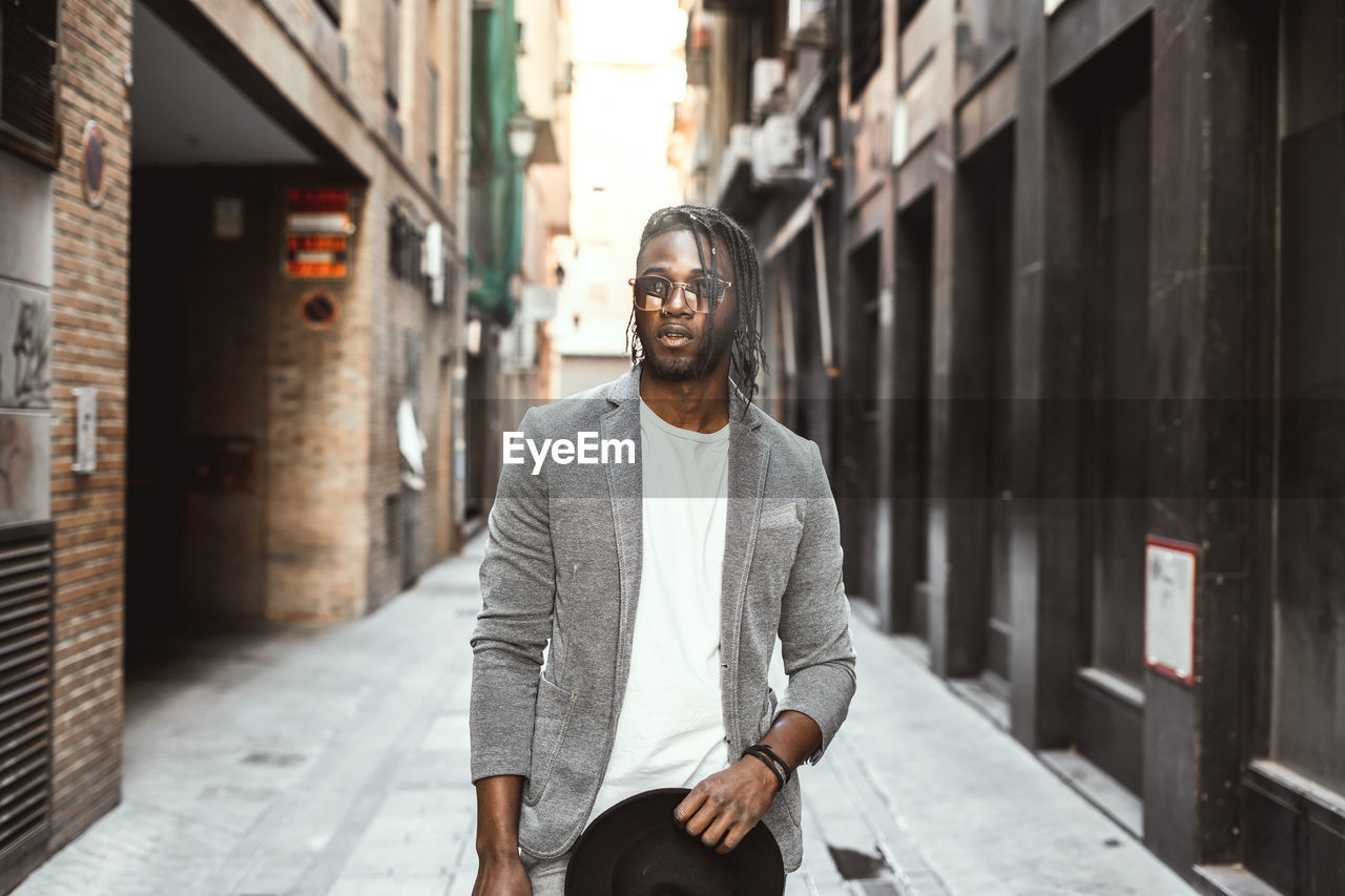 Young man wearing sunglasses standing at alley against building in city