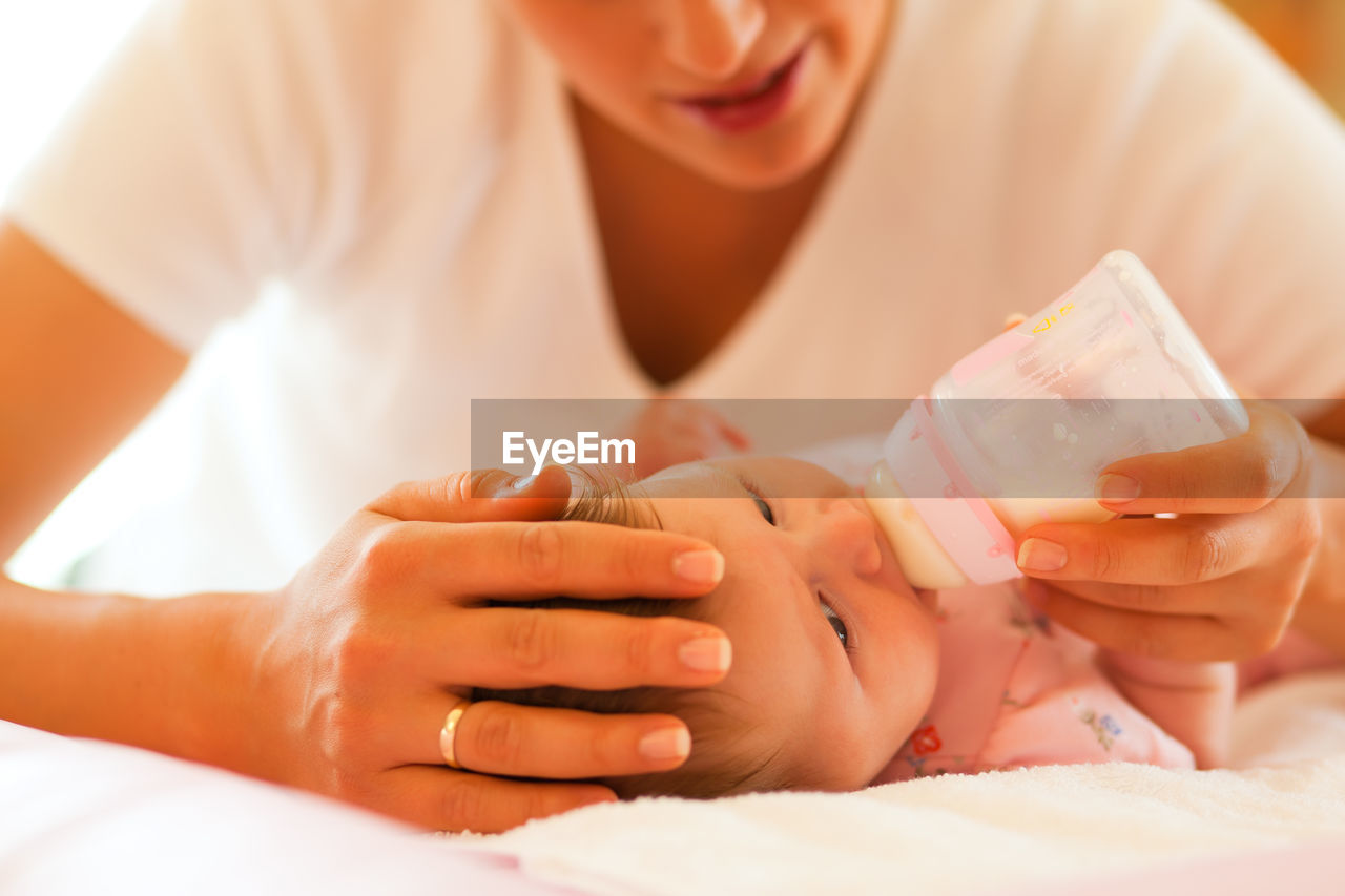 Midsection of woman feeding baby on bed