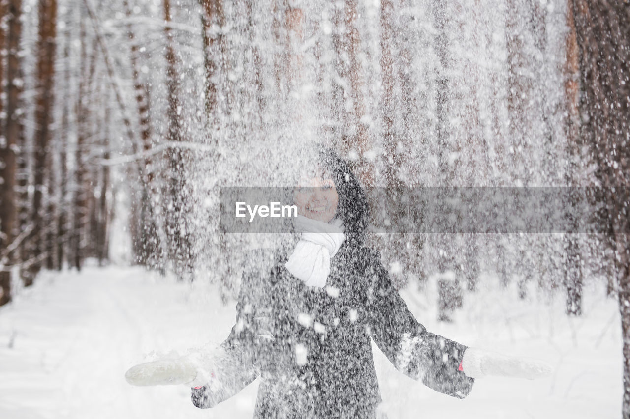 Smiling woman throwing snow mid air during winter